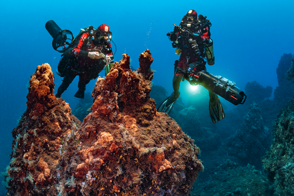Gombessa team divers Antonin Guilbert and Thibault Rauby are taking gas and freshwater samples from the active chimneys in The Valley of 200 Volcanoes. At a depth of 80 m, the divers only allow themselves one hour of work on the bottom, as this in turn will involve an ascent lasting more than three hours because of the mandatory decompression stops. The reddish-yellow colour of the chimneys is caused by the iron oxides, which crystallise upon contact with the cold water of the depths.
